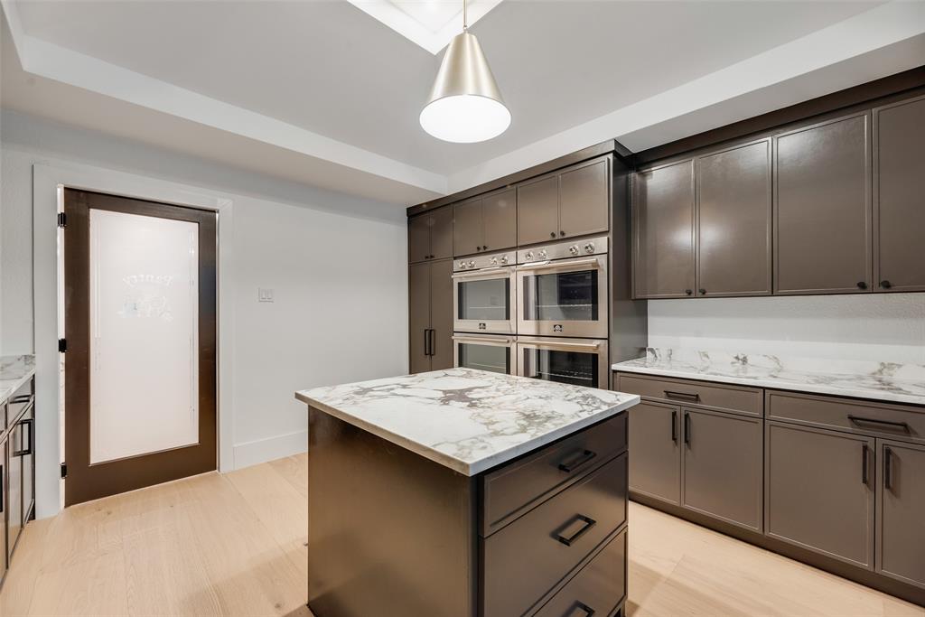 Kitchen featuring dark cabinetry, stone-surface countertops, built-in double wall ovens, a central island, and a frosted glass door