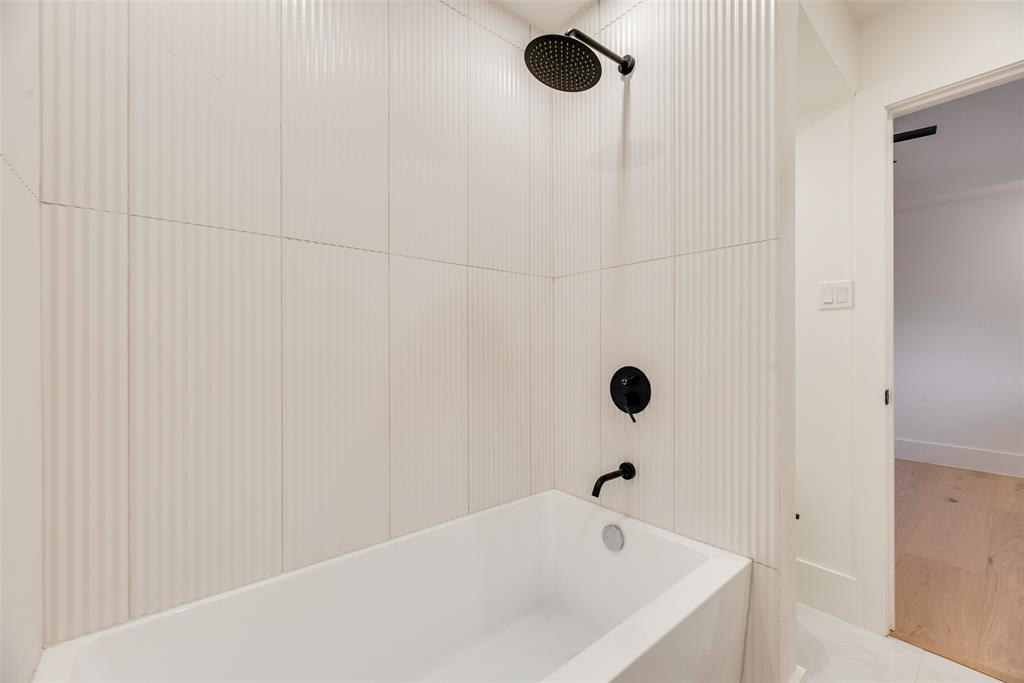 Full-height vertical fluted wall tiling surrounding a white soaking tub with matte black fixtures, including a round rainfall shower head and wall-mounted tub faucet