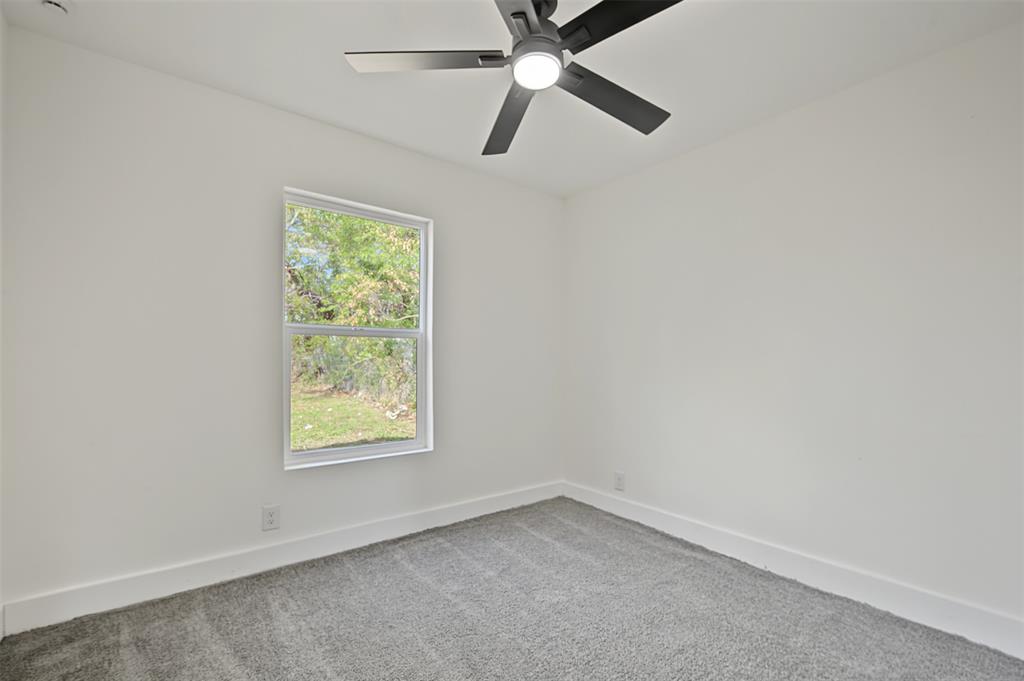 Neutral-toned interior featuring grey wall-to-wall carpeting, white walls, a single-hung window, and a matte black ceiling fan with integrated LED lighting