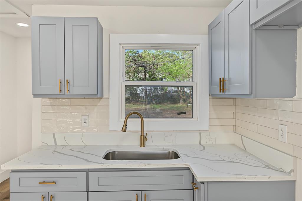 Kitchen featuring Shaker-style cabinetry, patterned stone-finish countertops, subway tile backsplash, stainless steel undermount sink, and brass-finish hardware