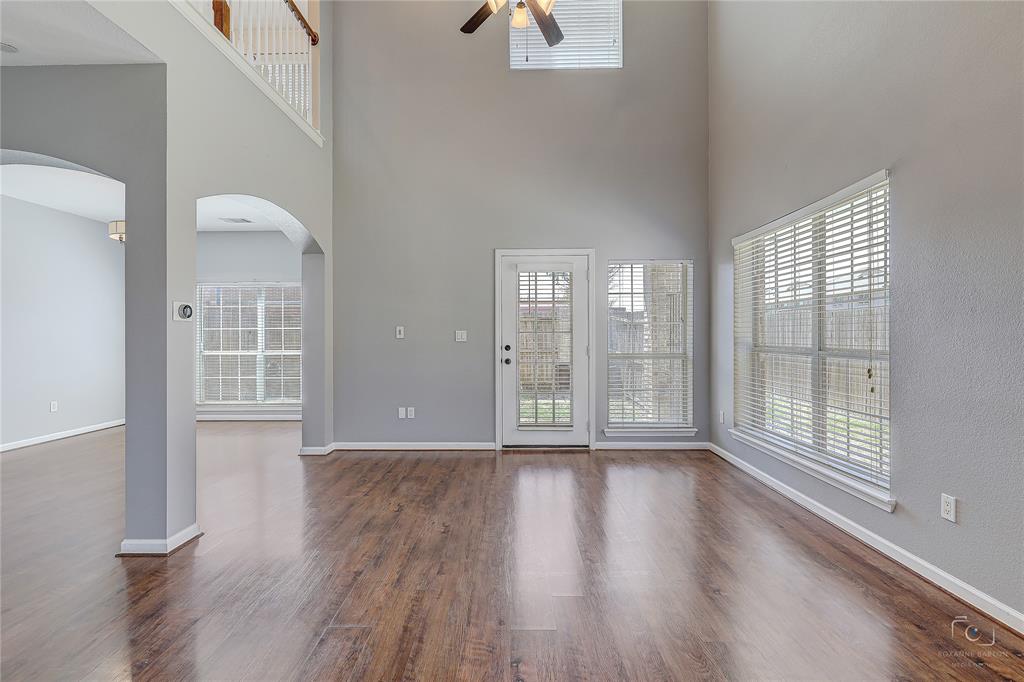 Two-story ceiling height, wood-finish flooring, arched architectural openings, natural light provided by expansive windows, and a ceiling-mounted fan