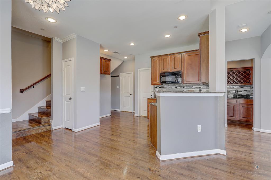 Wood-finish flooring, recessed lighting, stained wood cabinetry, stone-tile backsplash, and built-in wine storage