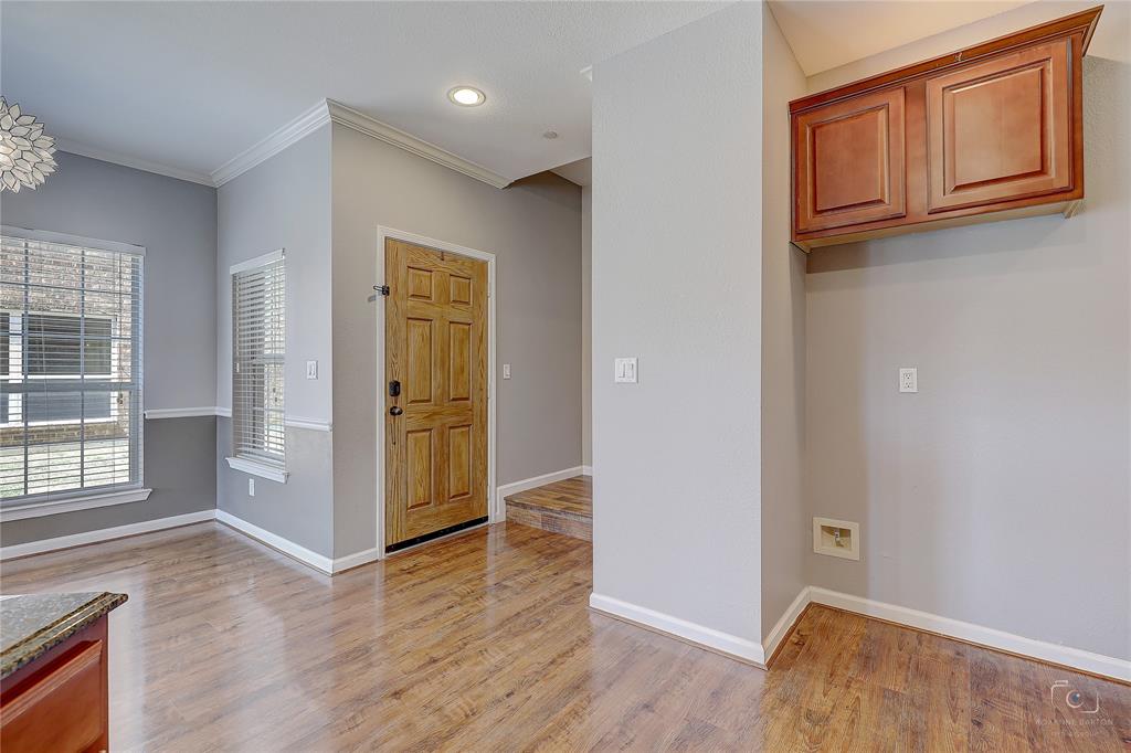 Interior space featuring wood-finish flooring, six-panel wood door, crown molding, wall-mounted cabinetry, and recessed lighting