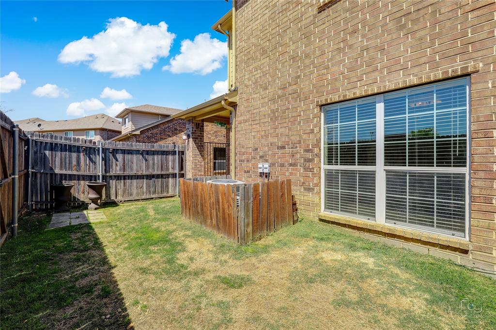 Exterior brick facade with a grid-patterned window, privacy fencing, and a side yard area