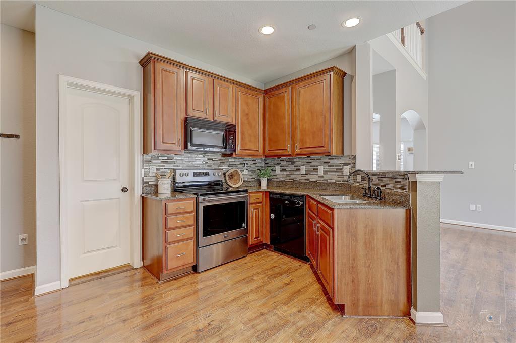 Kitchen featuring shaker-style wood cabinetry, stainless steel appliances, stone-finish countertops, decorative tile backsplash, and wood-finish flooring