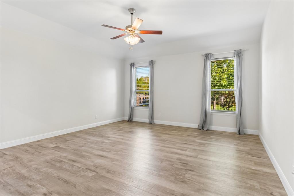 Spacious room featuring wood-finish flooring, dual windows, and a ceiling fan with integrated lighting