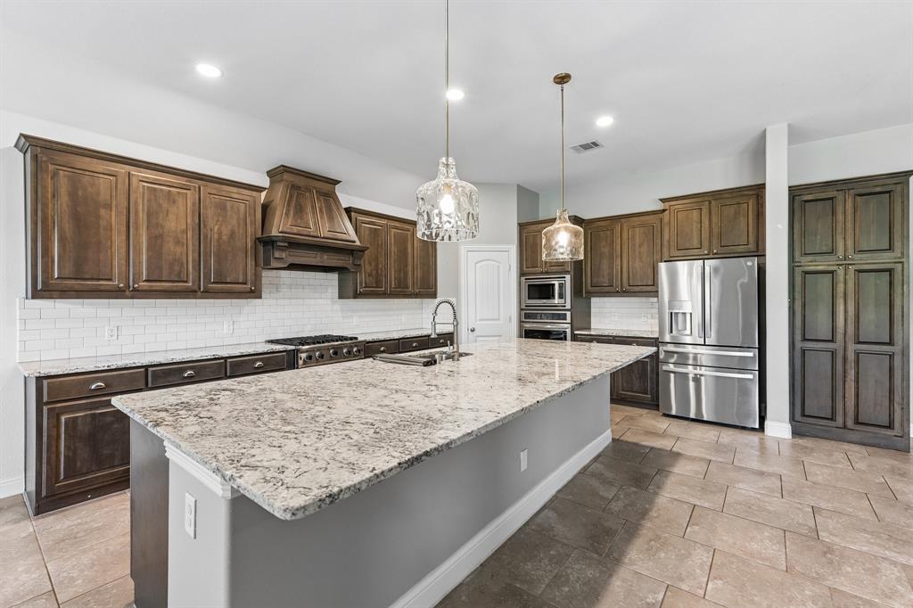 Kitchen featuring custom-stained cabinetry, stone countertops, a large center island, stainless steel appliances, and subway tile backsplash