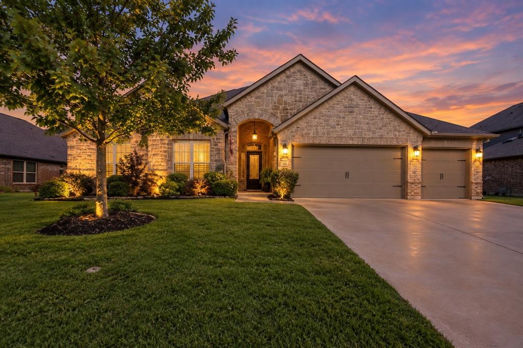Stone masonry exterior, arched entryway, multi-car garage, concrete driveway, and manicured landscaping
