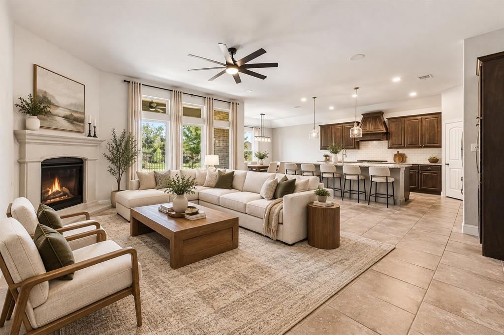 Open-concept interior featuring large-format tile flooring, a fireplace with a decorative mantel, tall windows, a kitchen island with stone countertops, and dark wood-finish cabinetry