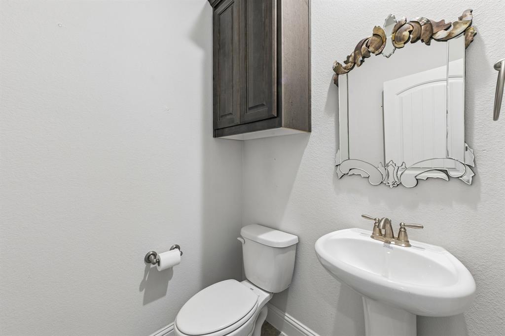 Wall-mounted dark wood-finish cabinet, pedestal sink with metallic two-handle faucet, and decorative arched wall mirror