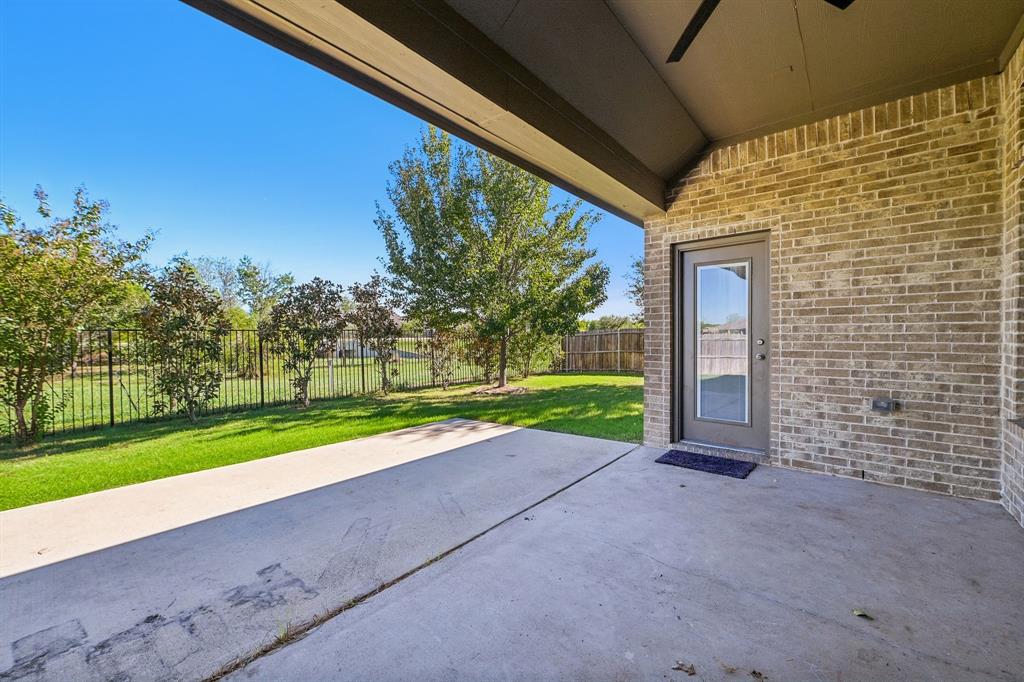 Covered concrete patio featuring brick exterior walls, a ceiling fan, and metal perimeter fencing bordering a lawn