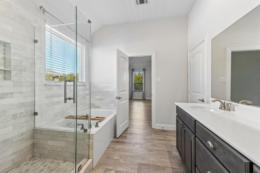 Bathroom featuring a glass-enclosed shower with tiled surround, separate soaking tub, wood-finish flooring, dark-toned cabinetry, and a countertop with an integrated sink