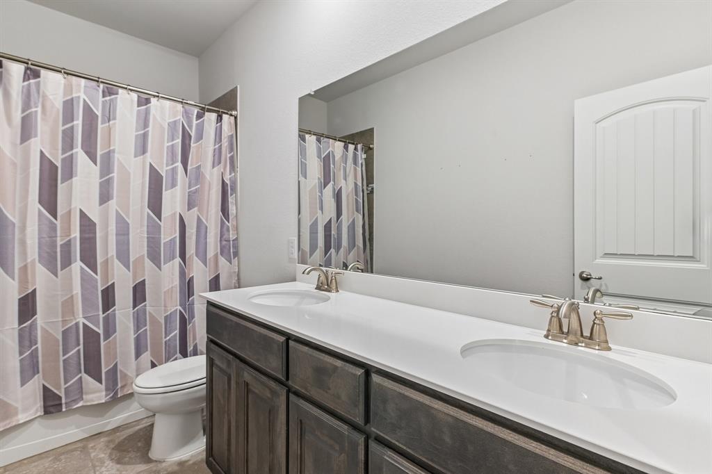 Dual-sink vanity with a solid-surface countertop, dark wood-finish cabinetry, a full-width wall mirror, and metallic finish hardware