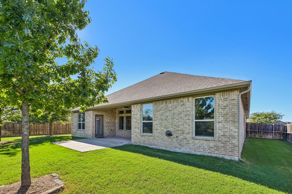 Brick exterior, rear concrete patio, and fenced yard with mature trees