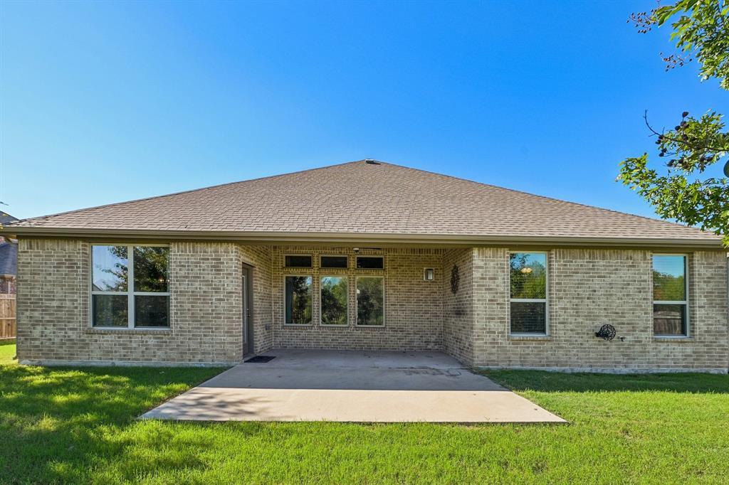 Rear exterior featuring a brick facade, concrete patio, multi-pane windows, and a hip roof