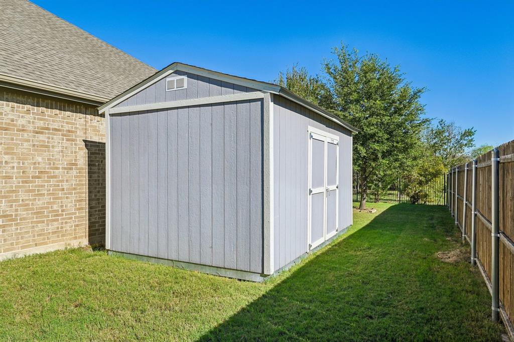 Exterior storage structure with vertical siding, gable roof, double-door entry, and wood fencing