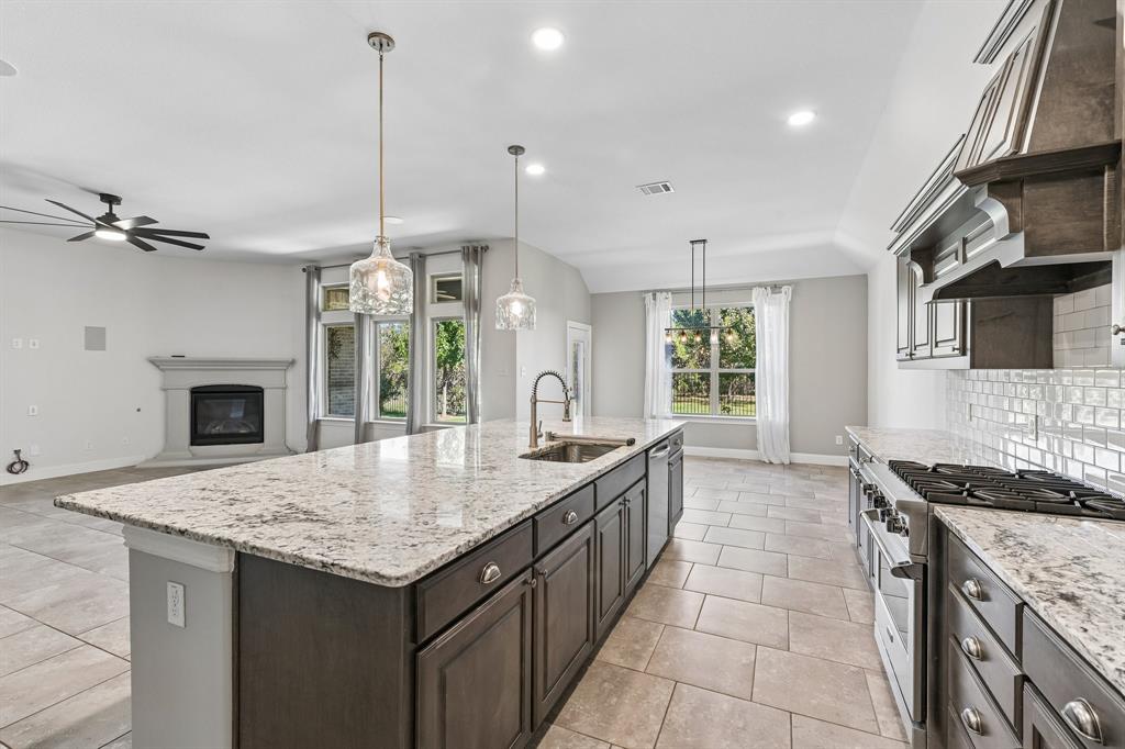 Kitchen featuring a large central island with light-toned stone countertops, dark cabinetry, tile flooring, built-in stainless steel appliances, and a tiled backsplash