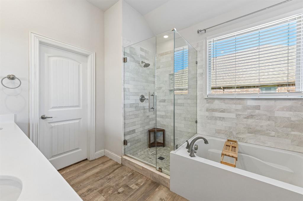 Glass-enclosed shower with horizontal wall tile and stone-finish floor, deep soaking tub with wall-mounted faucet, and wood-finish flooring