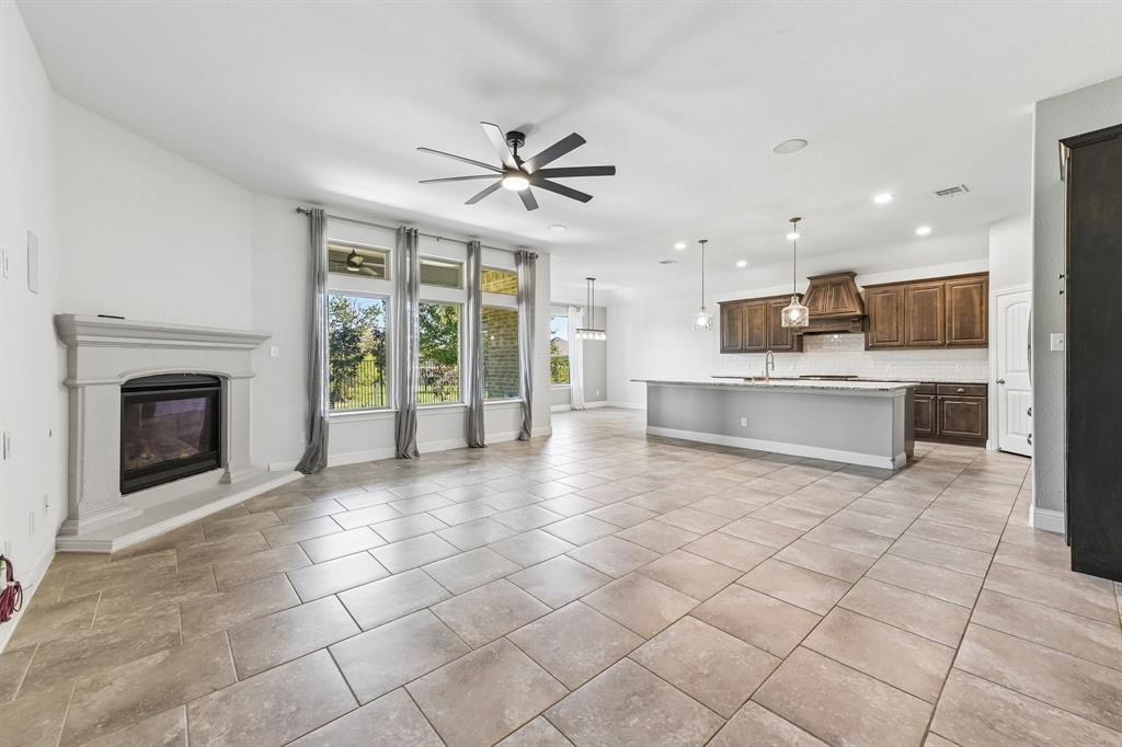 Open-concept interior featuring large-format tile flooring, a stone-finish fireplace surround, dark wood cabinetry with a coordinating range hood, and a kitchen island with stone-finish countertops
