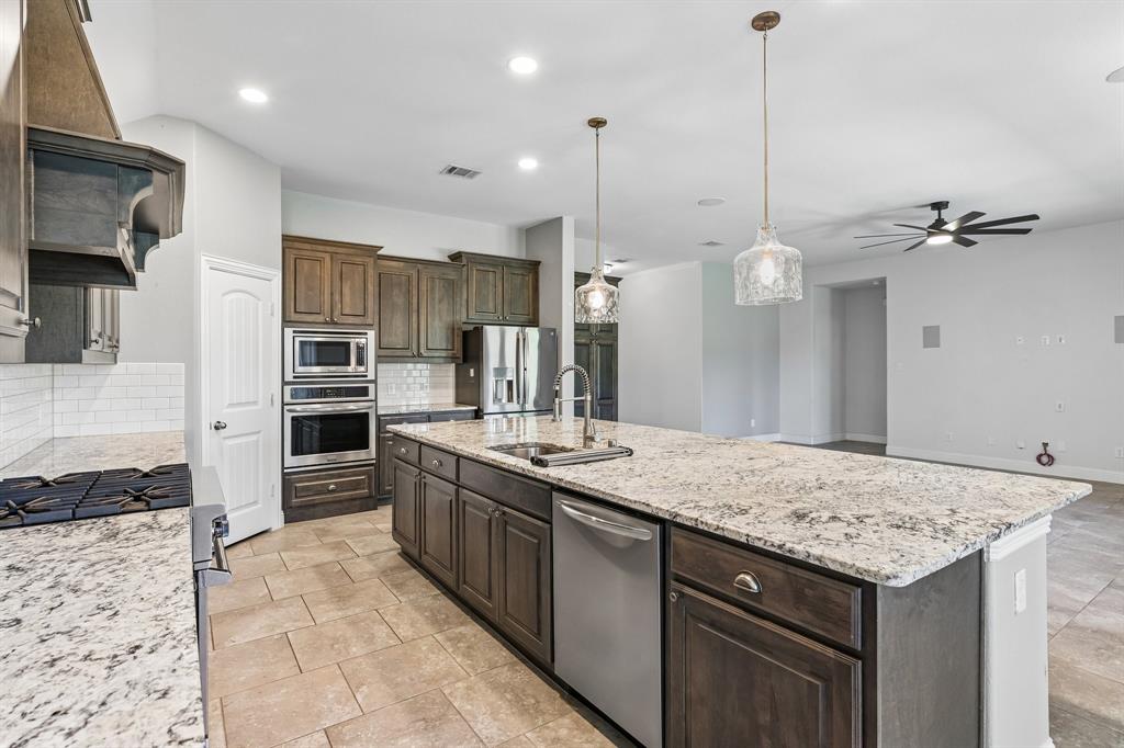 Kitchen featuring stone countertops, dark-finish cabinetry, stainless steel double wall ovens, a large central island, and glass pendant lighting