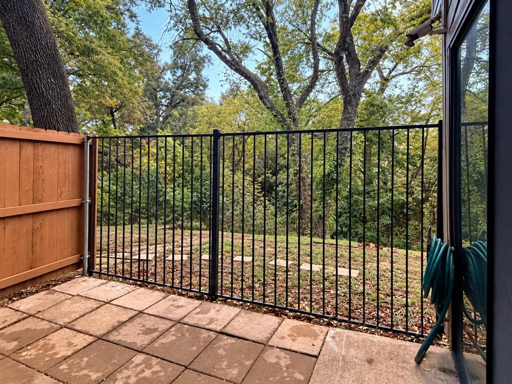 Concrete paver patio featuring black metal perimeter fencing, wood privacy screen, and stone stepping stones