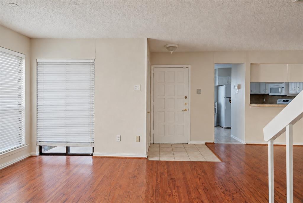 Wood-finish flooring, tiled entryway, white paneled front door, and white staircase railing