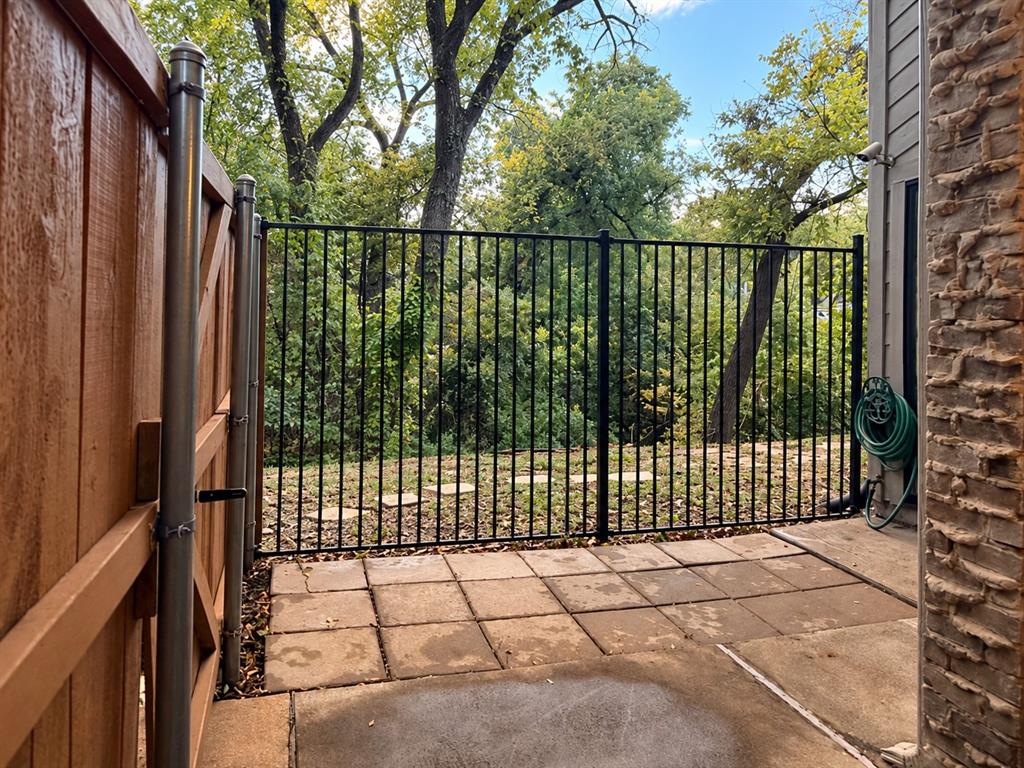 Concrete paver patio featuring a black metal perimeter fence, solid wood privacy fencing, and masonry exterior wall