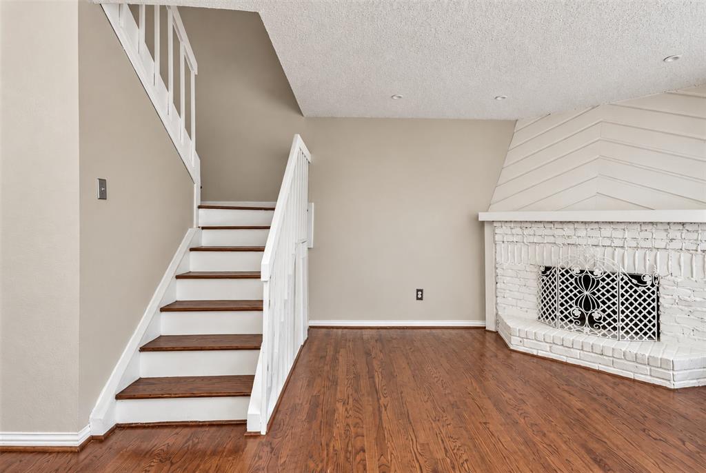 Wood-finish flooring, staircase with white railing and wood-finish treads, and a white painted brick fireplace with geometric wall paneling