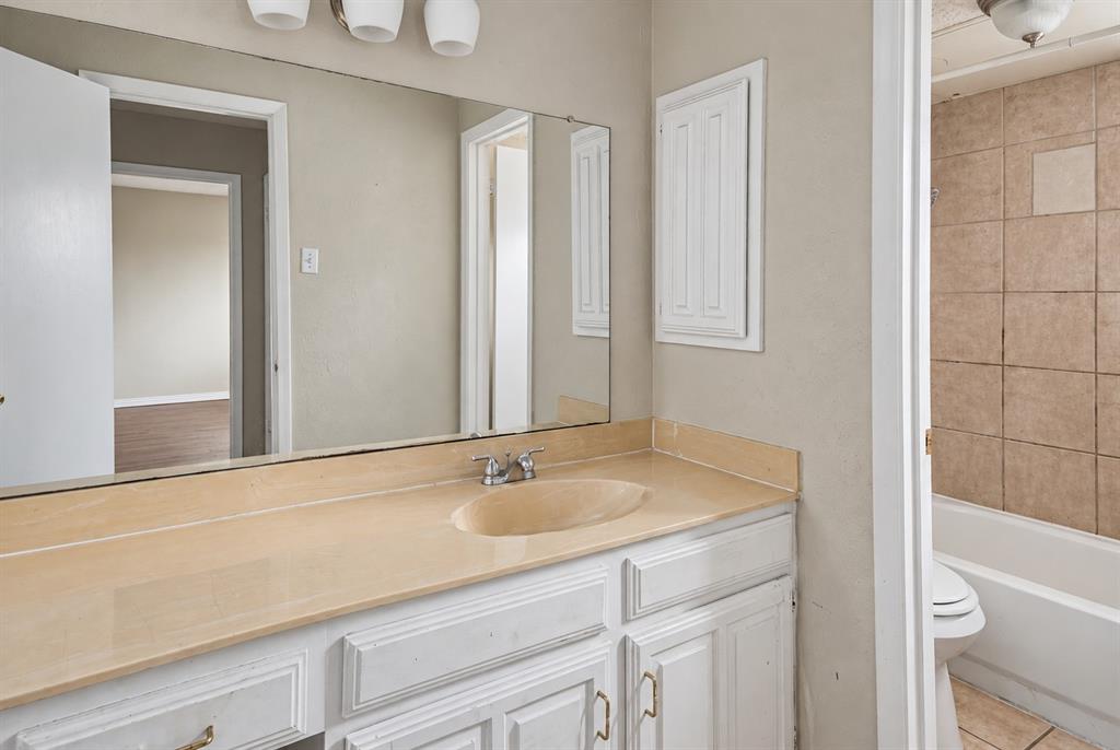 Bathroom vanity featuring white cabinetry, a solid-surface countertop with an integrated oval sink, a large wall-mounted mirror, and a three-light fixture