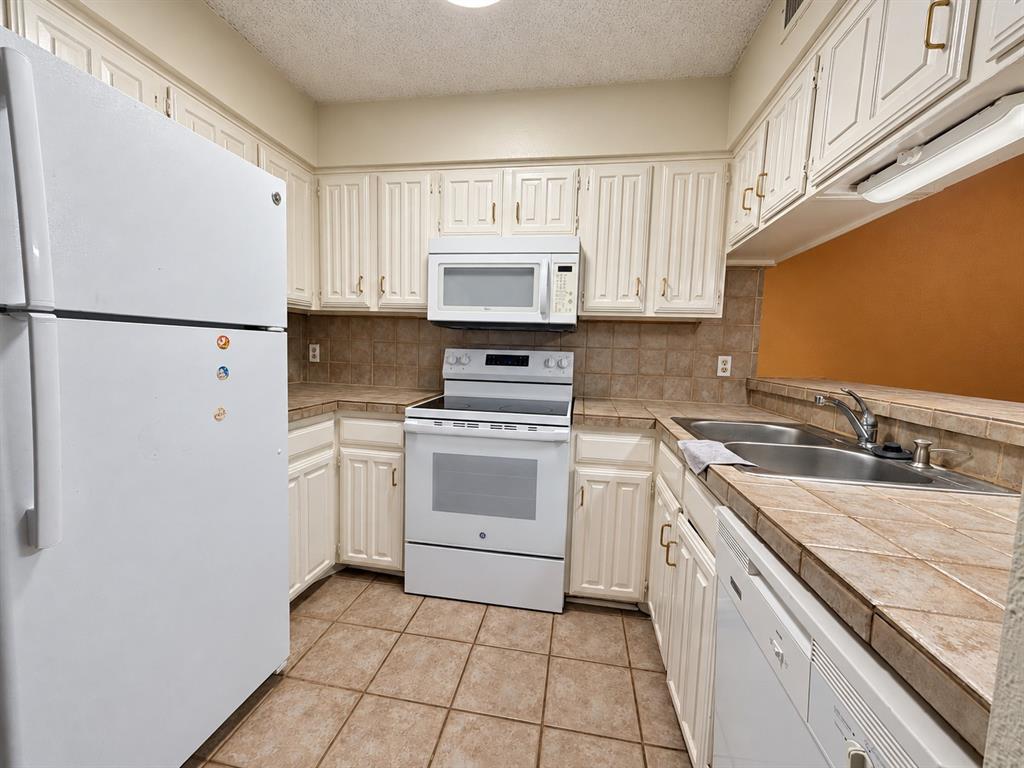 Kitchen featuring white cabinetry, tile countertops and backsplash, tile flooring, and white built-in appliances including a refrigerator, electric range, microwave, and dishwasher