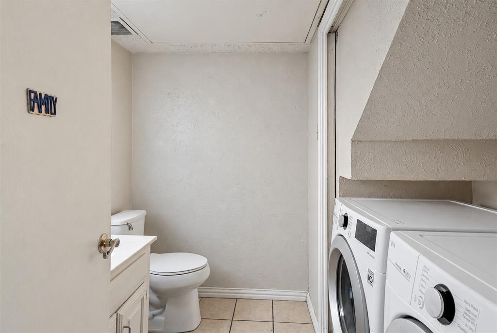 Full bathroom featuring tile flooring, a white vanity cabinet, a commode, and dedicated space for laundry appliances