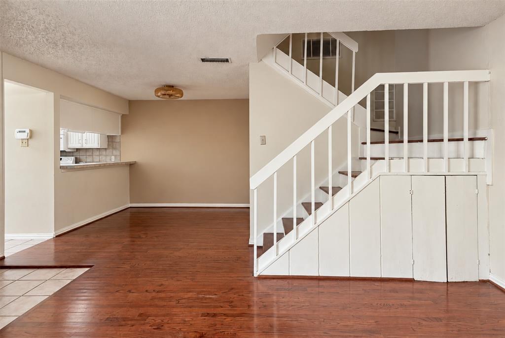 Wood-finish flooring throughout common area, white staircase with vertical balusters, and integrated under-stair storage cabinetry