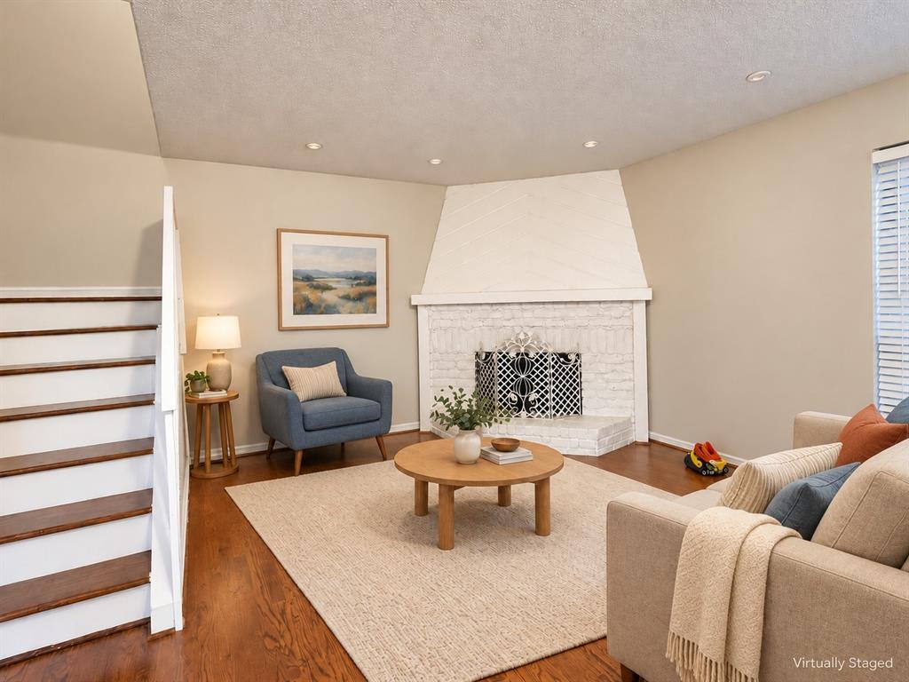 Corner fireplace with a painted brick surround and diagonal wood-paneled accent, wood-finish flooring, and recessed ceiling lighting