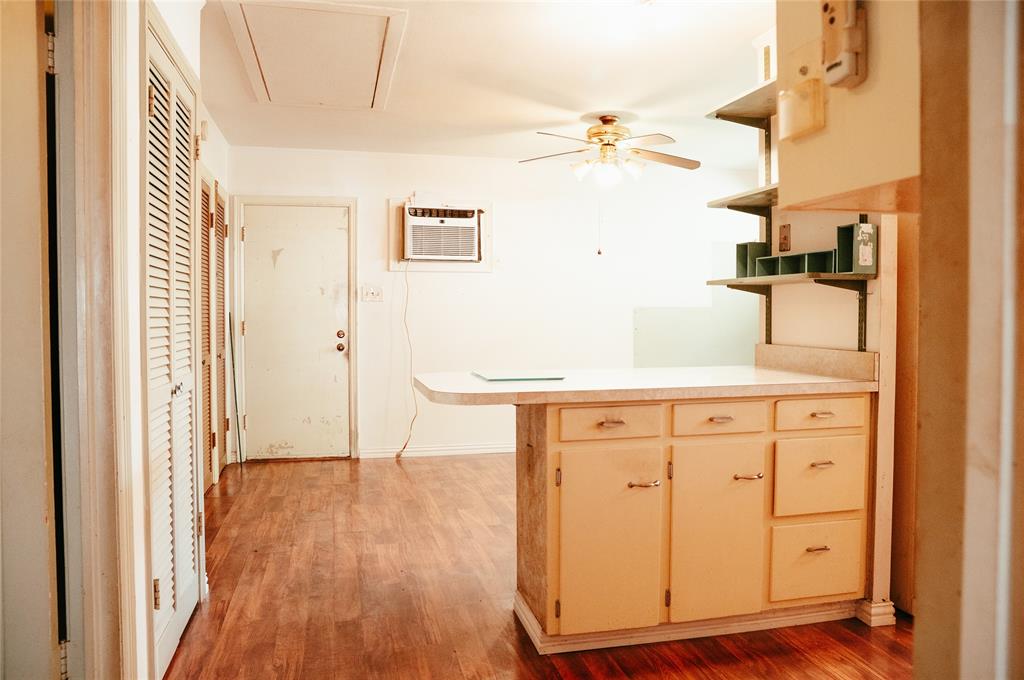 Kitchen area featuring wood-finish flooring, a breakfast bar with cabinetry, integrated wall shelving, a ceiling fan, and a wall-mounted air conditioning unit