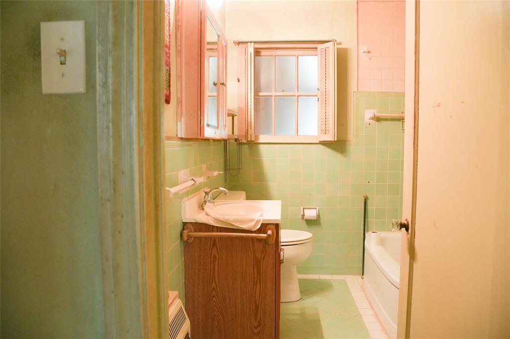 Bathroom featuring wall-mounted cabinetry, a wood-finish vanity, a window with louvered shutters, and tiled wall surfacing