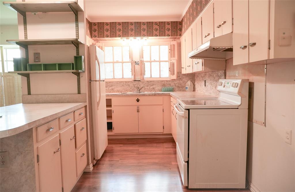 Kitchen featuring wood-finish flooring, white cabinetry, integrated range hood, double-window configuration, and an open-shelf workstation