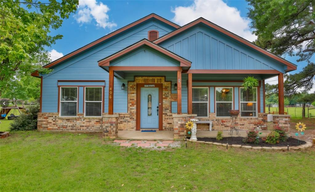 Single-story exterior featuring blue vertical siding, brick veneer foundation, front-facing gabled roofline, and a covered porch supported by wood-finish posts
