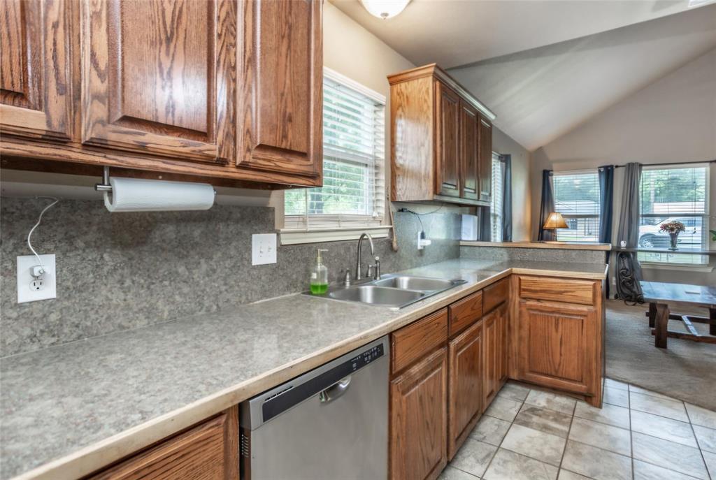 Kitchen featuring stained wood cabinetry, stone-finish countertops, tile flooring, stainless steel dishwasher, and vaulted ceilings