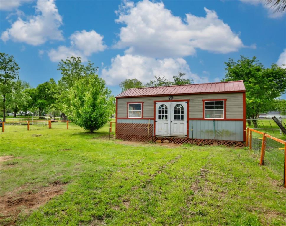Detached storage structure with a metal roof, double-door entry, multi-pane windows, and lattice skirting, situated within a fenced exterior space