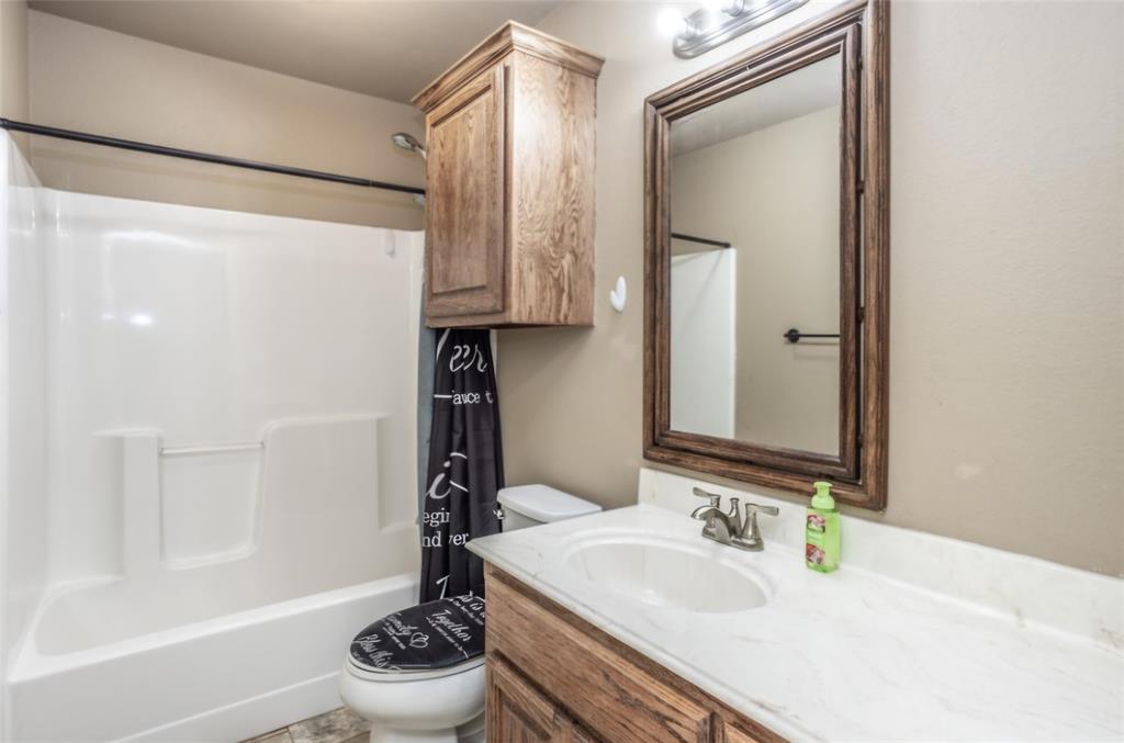 Bathroom featuring a white molded tub-shower surround, wood-finish vanity with a stone-composite countertop, matching wall-mounted cabinet, and wood-framed vanity mirror