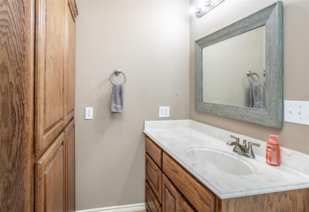 Vanity featuring wood-finish cabinetry, integrated countertop with molded sink, chrome dual-handle faucet, wall-mounted mirror, and floor-to-ceiling built-in storage cabinet