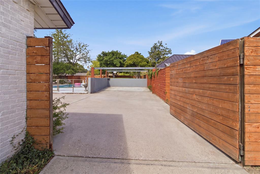 Beyond the horizontal wood privacy gate, the extended driveway opens into a generous paved parking area, offering convenient additional parking for vehicles and guests. The wood fencing complements the home's contemporary styling while providing separation from the street. With the swimming pool and outdoor entertaining areas nearby, this flexible space is especially convenient when hosting larger gatherings.