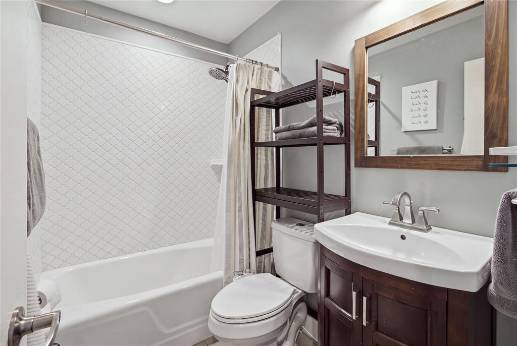 30. The second full bathroom is conveniently located off the hallway, serving both secondary bedrooms and guests. Features include a tub and shower combination with decorative tile surround, a dark wood vanity, and a coordinating framed mirror.