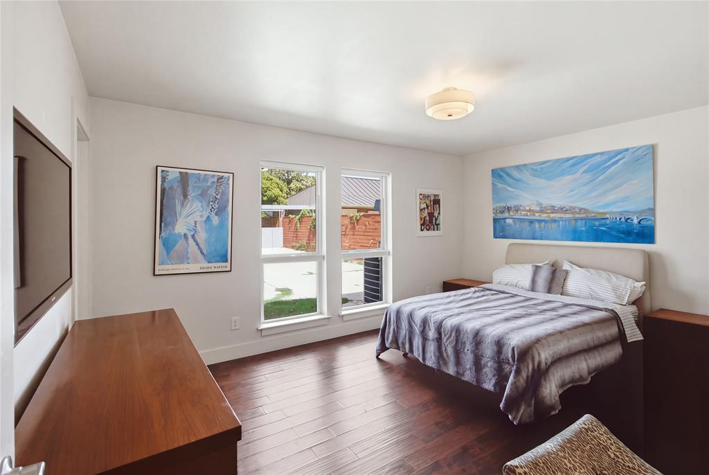 The spacious primary bedroom welcomes natural light through two large windows overlooking the backyard. Rich, warm-toned flooring, neutral walls, and ample space for bedroom furnishings create a comfortable retreat with a clean, contemporary feel.