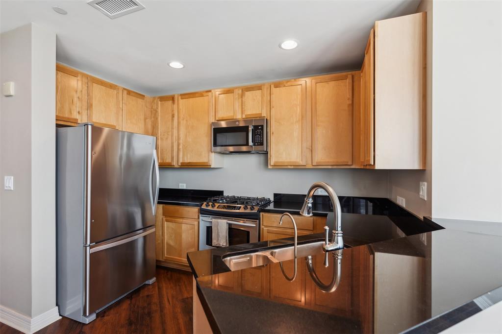 Kitchen featuring wood-finish cabinetry, black stone countertops, stainless steel appliances, a gas range, and a double-basin stainless steel sink with a high-arc faucet