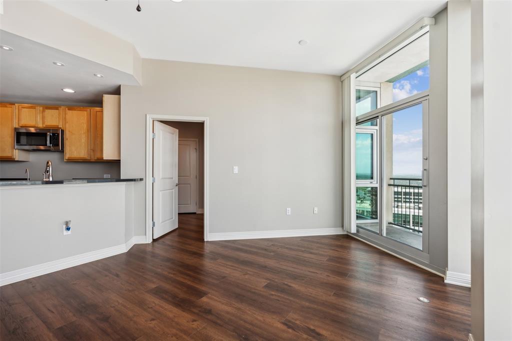 Open-concept living space featuring wood-finish flooring, floor-to-ceiling windows, access to a private balcony, and a kitchen with wood cabinetry and a breakfast bar