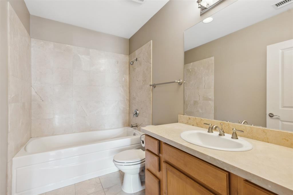 Bathroom featuring a vanity with an integrated basin, tile-surround bathtub, large wall-mounted mirror, and metal fixtures