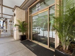 Building entrance featuring glass-paneled double doors, metal framing, a covered exterior walkway, and stone-finished structural pillars