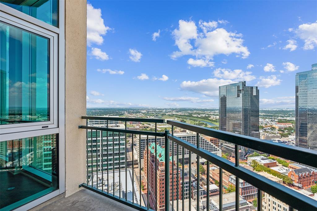 Private balcony with metal railing, floor-to-ceiling glass windows, and panoramic urban cityscape