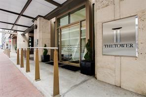 Building entrance featuring a covered pedestrian walkway, natural stone facade, glass-paneled doors, and metal-finished signage